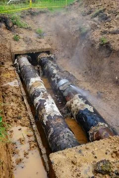 Exposed damaged heating pipelines in open trench with steam and muddy repai.. Stock Photos