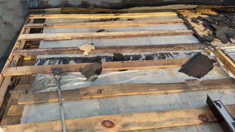 Exposed roof structure with damaged shingles, wooden battens, and weathered Stock Footage 346756950