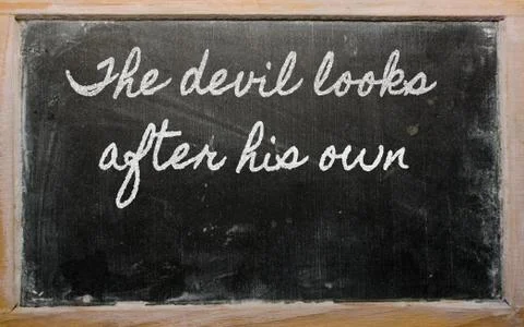 Expression -  the devil looks after his own - written on a school blackboard  Stock Photos