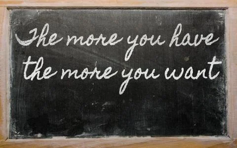 Expression -  the more you have, the more you want - written on a school blac Stock Photos