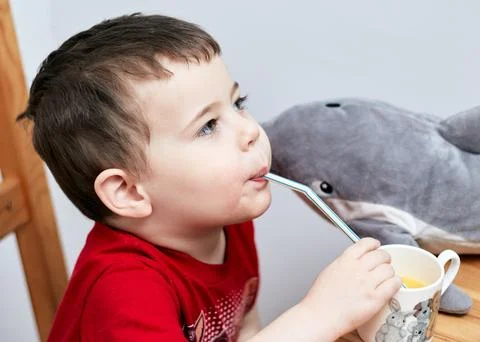 Expressive boy drinking orange juice through a plastic straw Foto stock