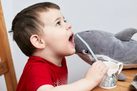 Expressive boy drinking orange juice through a plastic straw Stock Photos