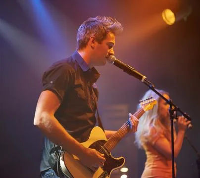 An expressive frontman singing and playing guitar at a gig. This concert was Stock Photos