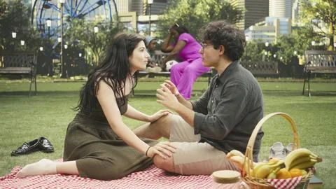 Expressive man gestures with both hands talking to woman seated on blanket Stock Photos