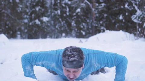 An expressive man pushing up on snow in a winter forest Stock Footage 101344842