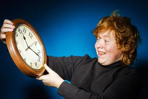 Expressive red-haired teenage boy showing time on big clock Stock Photos