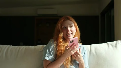 Expressive redhead woman using smartphone on sofa Stock Footage 334636352