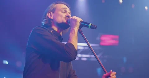 Expressive singer singing into microphone. Live music concert in front of bright Video stock 154333427