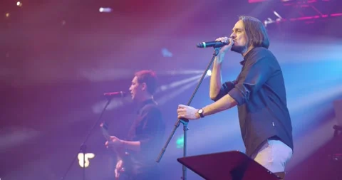 Expressive singer singing into microphone. Live music concert in front of bright Video stock 154353168