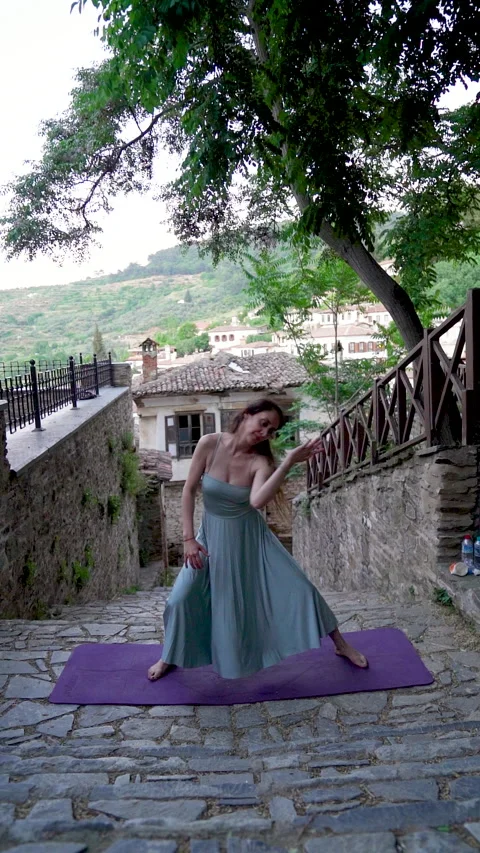 Expressive woman doing creative dance yoga flow on a historic village street Stock Footage 336139917