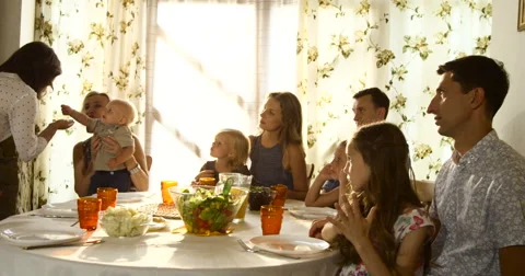 Extended family group sitting down to meal and looking at grandmother holding Stock Footage 66290175
