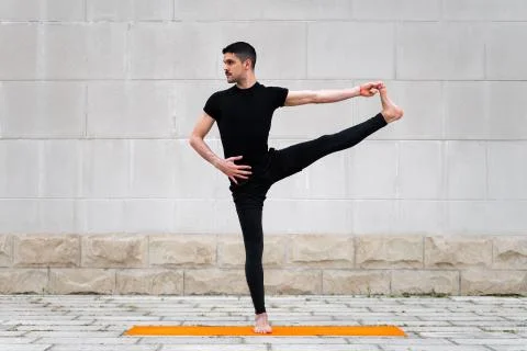 Extended Hand to Big Toe pose. Attractive latin man doing yoga outdoors in a Stock Photos