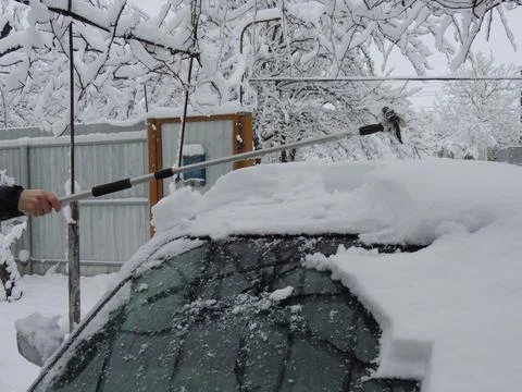Extended scraper in hand cleaning snow from car against snowy yard background Foto stock