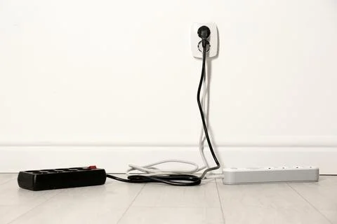Extension cords with power plugs in socket indoors, space for text. Electrici Stock Photos