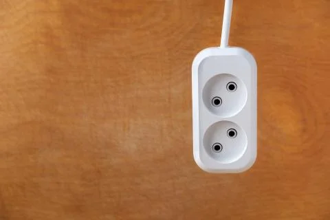 The extension socket hangs against the background of a wooden wall. Stock Photos