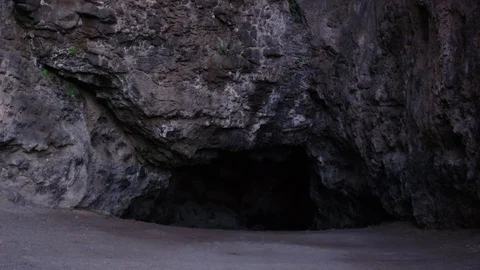 Exterior view of a cave opening in dark gray volcanic rock face, lock off. Stock Footage 80512164