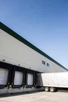 Exterior view of a warehouse loading dock with a truck trailer pulled up to one Stock Photos