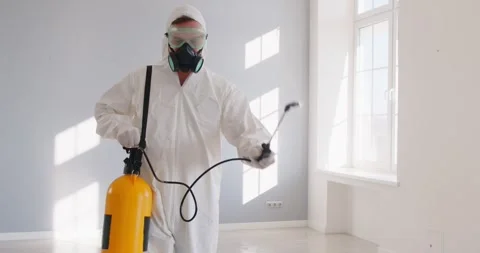 Exterminator in white protective suit spraying pesticide in bright modern room Stock-Footage 329875491