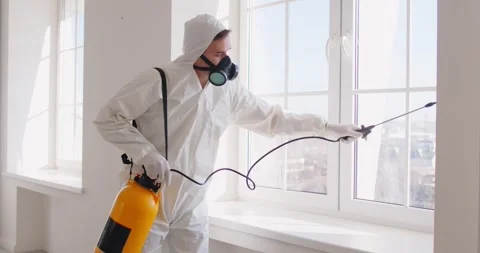 Exterminator in white protective suit spraying pesticide during indoor pest Vidéo 330631439