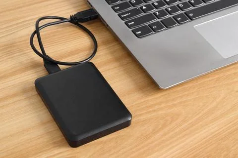 External backup hard disk drive connected to laptop on wooden table Stock Photos