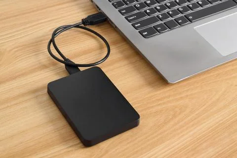 External backup hard disk drive connected to laptop on wooden table Stock Photos