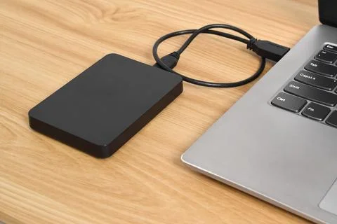 External backup hard disk drive connected to laptop on wooden table Stock Photos