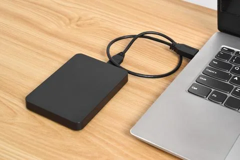 External backup hard disk drive connected to laptop on wooden table Stock Photos