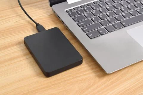 External backup hard disk drive connected to laptop on wooden table Stock Photos