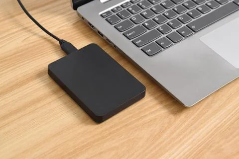 External backup hard disk drive connected to laptop on wooden table Stock Photos