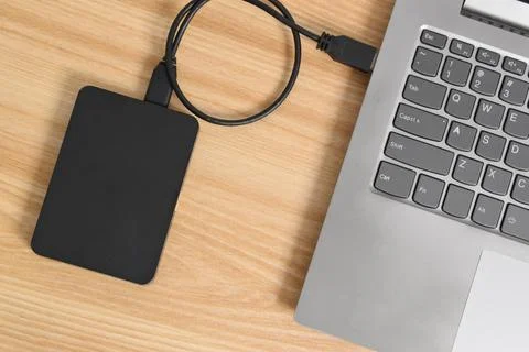 External backup hard disk drive connected to laptop on wooden table Stock Photos