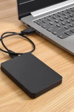 External backup hard disk drive connected to laptop on wooden table Stock Photos