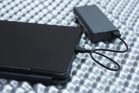 External battery connected by a USB cable to a tablet in a black case. Concep Stock Photos