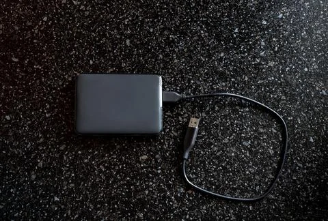 External hard drive in a black case with a wire on a black background. Useful Stock Photos