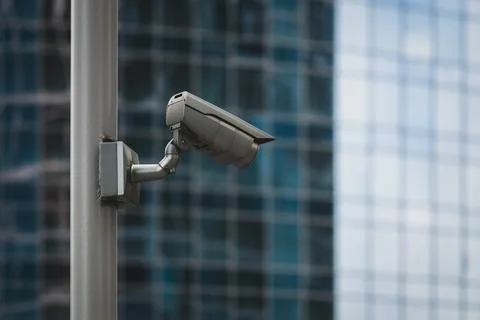 External security camera on pole in front of glass building wall Stock Photos
