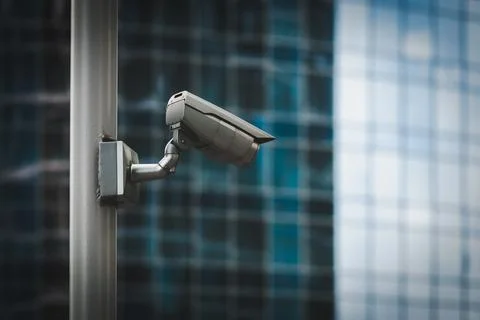 External security camera on pole in front of glass building wall Stock Photos