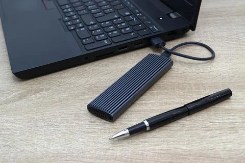 External Solid State Drive Connected to Laptop with Black Pen on Wooden Table Stock Photos