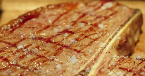 Extra close-up of ready T-bone meat steak sprinkled with large salt on wooden Stock Footage 271090660