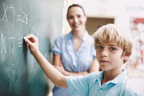 Extra lessons. A young boy doing mathematics on the blackboard as his teacher Stock Photos