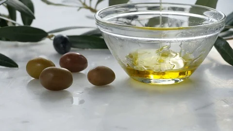 Extra Virgin oil falls on transparent bowl, white background. Genuine Italian in Stock Footage 122495589