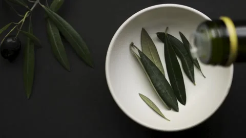 Extra virgin olive oil drops on leaves in white bowl black background Stock Footage 334681815