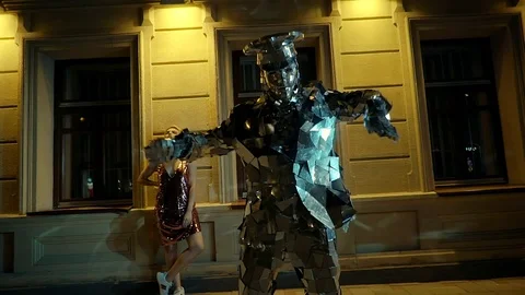 Extravagant man in mirror suit is dancing in night in street, girl in background Stock Footage 93000080