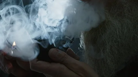 Extreme close up: Backlit bearded man lights, smokes pipe in darkness Video stock 310298778