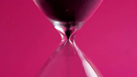 Extreme close-up of black sand running down through hourglass on a crimson Stock Footage 137769872