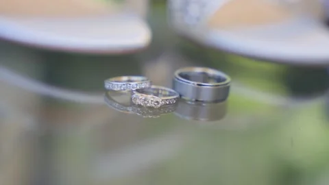 Extreme Close-Up of Diamond Wedding Ring Set and Groom's Band on Reflective Stock Footage 333973994