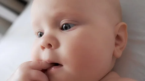 Extreme close up face of cute newborn baby putting finger in mouth lying on cozy Stock Footage 129680978