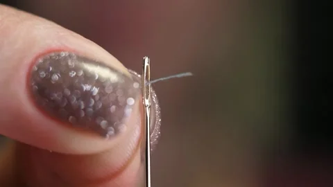 Extreme close-up of female hands insert a gray thread into the hole of a needle Stock Footage 262250565