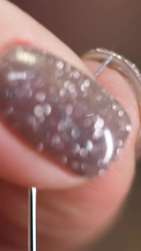 Extreme close-up of female hands insert a gray thread into the hole of a needle Stock Footage 324791346