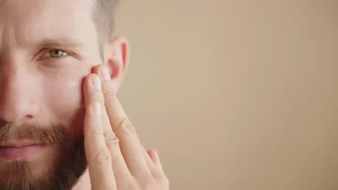 Extreme close-up, half face young man 30s, applying facial moisturizer Stock Footage 250659194