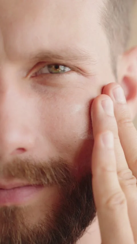 Extreme close-up, half face young man 30s, applying facial moisturizer Stock Footage 250669204
