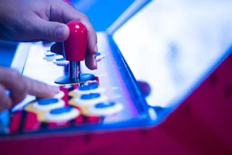 Extreme close-up of a hand on a red arcade joystick in blue light Stock Photos